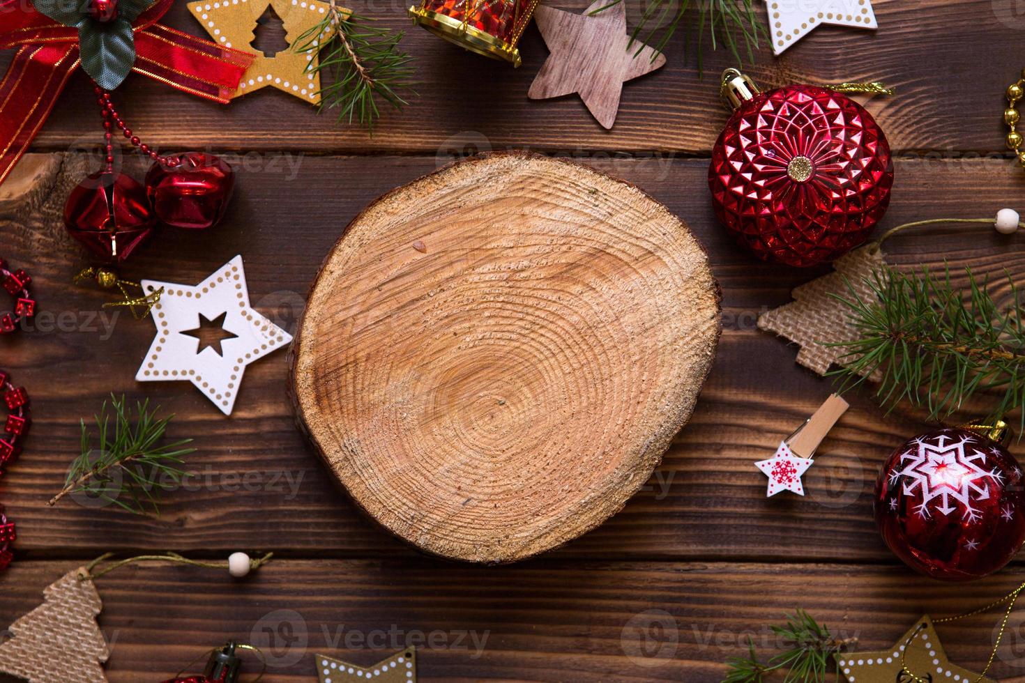 Christmas flat lay of red balloons and wooden stars and clothespins on a dark background with tree trunk section for notes in center. New year's frame, space for text. Xmas toys, beads, pine branches photo