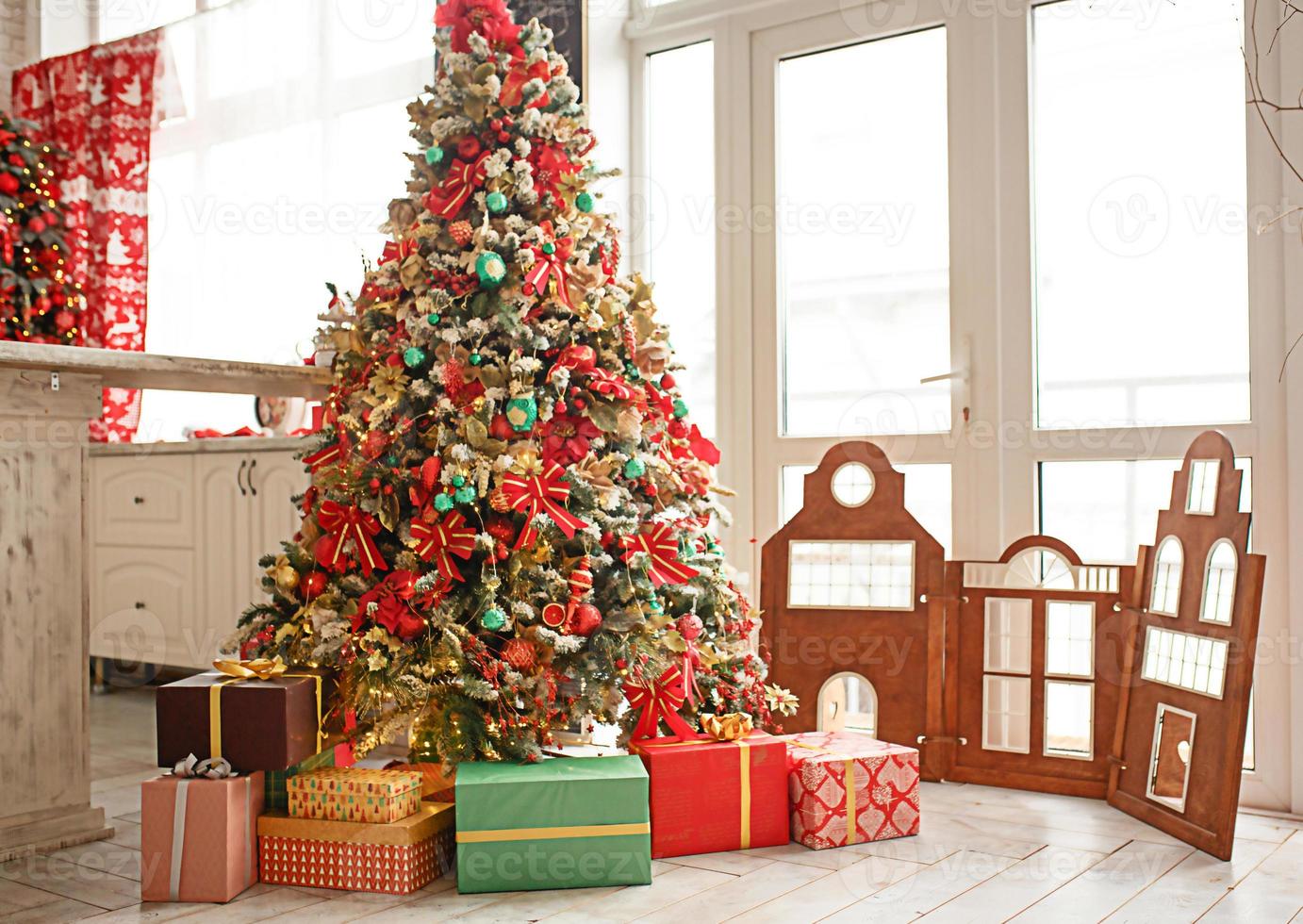 The Christmas tree is decorated with red and green toys, boxes with gifts on the floor. New year's atmosphere in the house, festive interior. photo