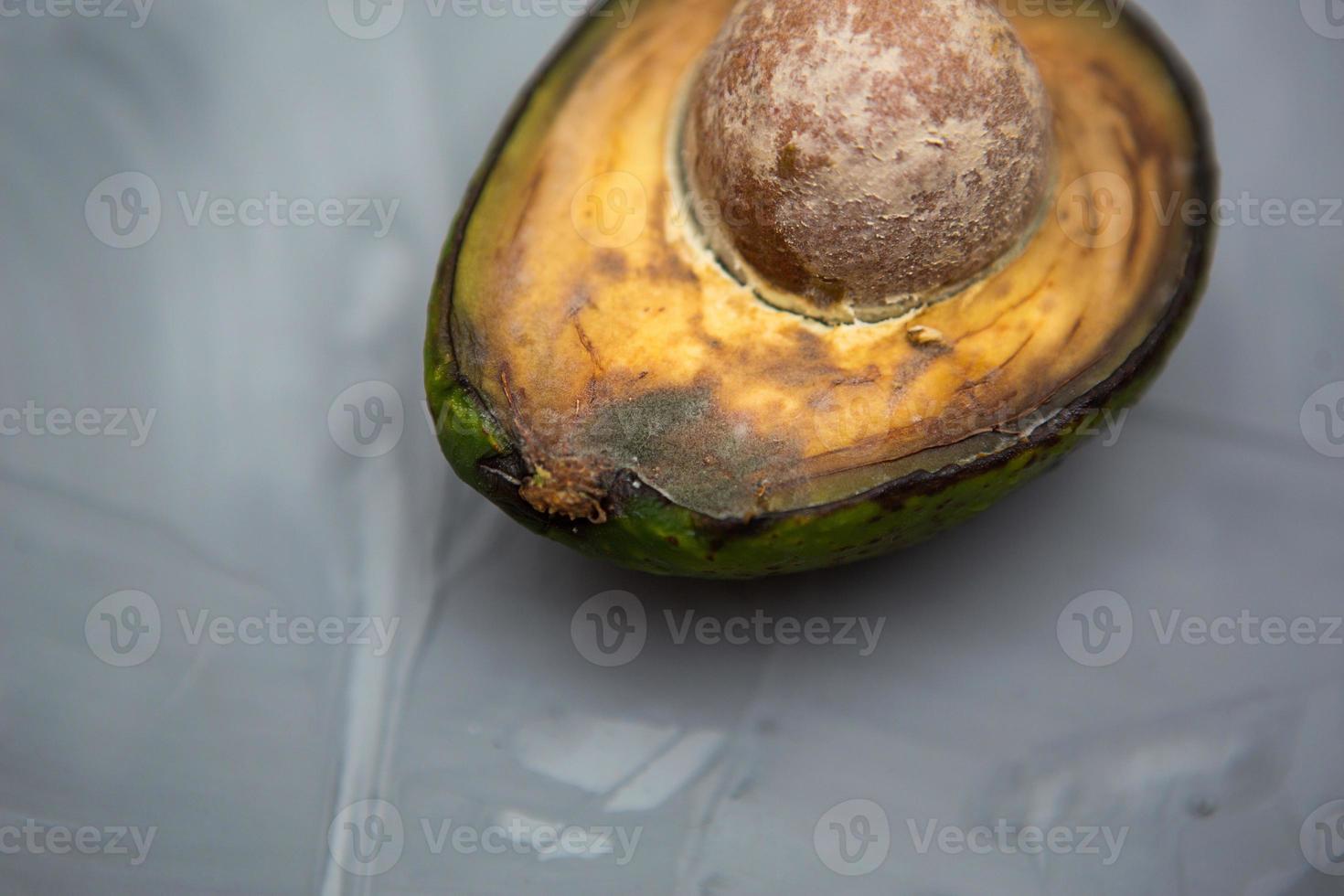 Spoiled avocado with green mold and black spots of rot and fungus on a gray background. Cut natural fruit, half with a round bone. Space for text photo