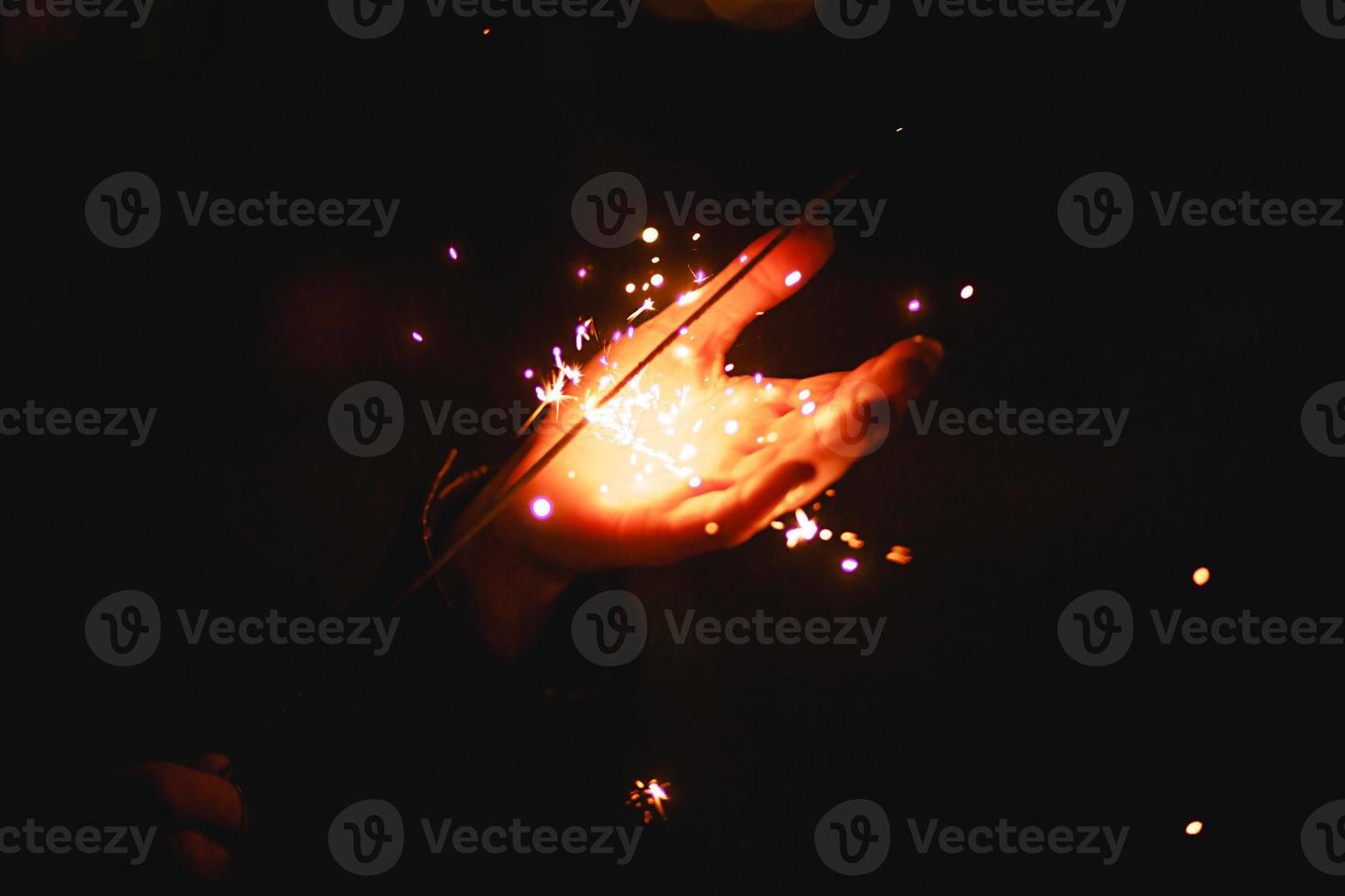 Sparks and light from sparklers in the dark on the palm of a person. Christmas magic, new year's eve, festive background. Space for text photo