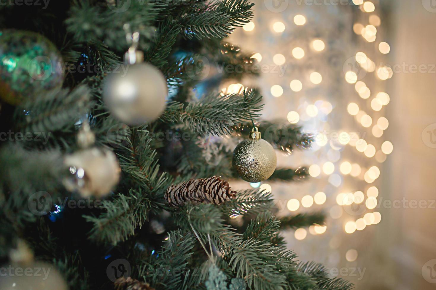 Silver Christmas decor on a green artificial fir tree with lights garlands in bokeh in the background. New year, Christmas toys, ball close-up. Space for text. photo