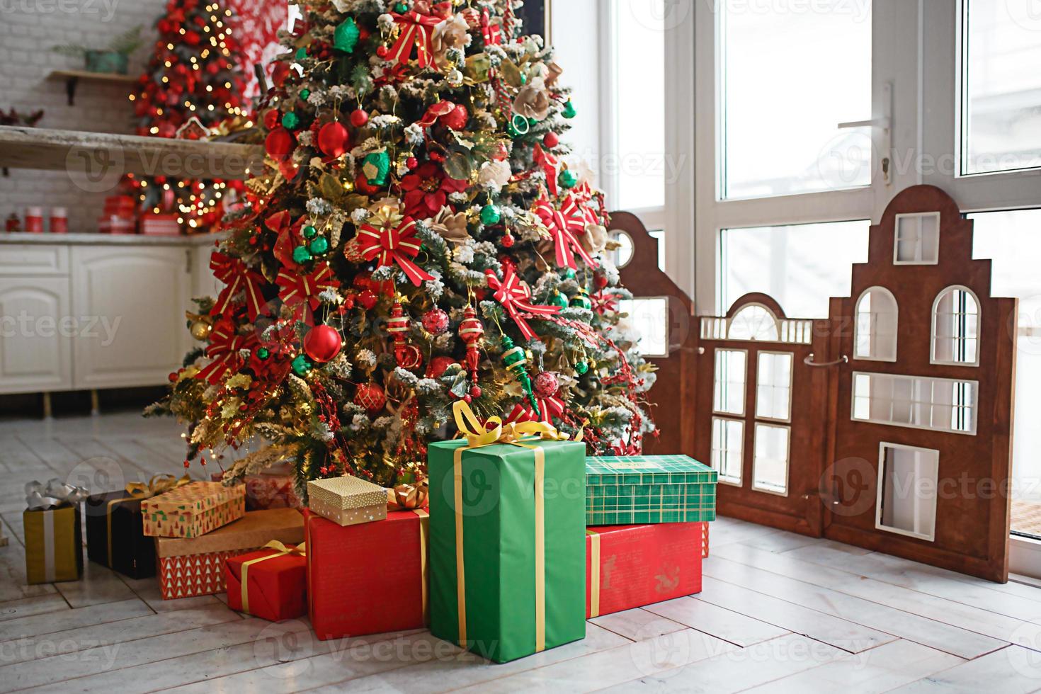 The Christmas tree is decorated with red and green toys, boxes with gifts on the floor. New year's atmosphere in the house, festive interior. photo