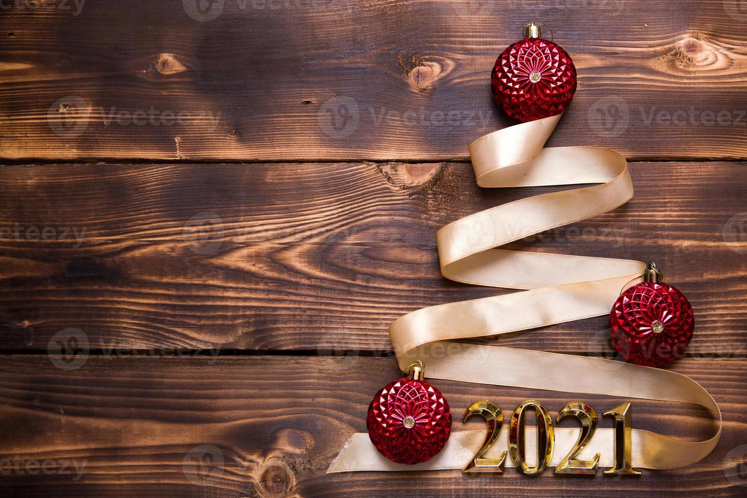 A Christmas tree made of gold ribbon with the numbers 2021 is decorated with red balloons on a dark wooden background. Flat lay. Space for text. New year, Santa hat. photo