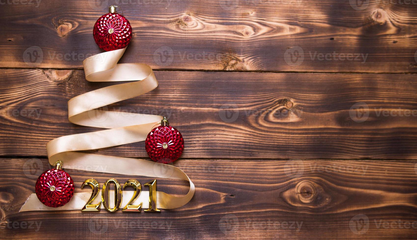 A Christmas tree made of gold ribbon with the numbers 2021 is decorated with red balloons on a dark wooden background. Flat lay. Space for text. New year, Santa hat. photo