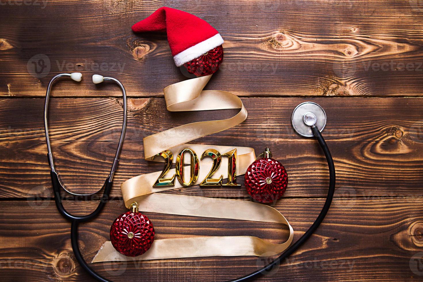 Christmas flat lay on a medical theme. Decorations for the new year from stars, ball, ribbons, Santa hats, and a doctor's stethoscope. Wooden background, space for text photo