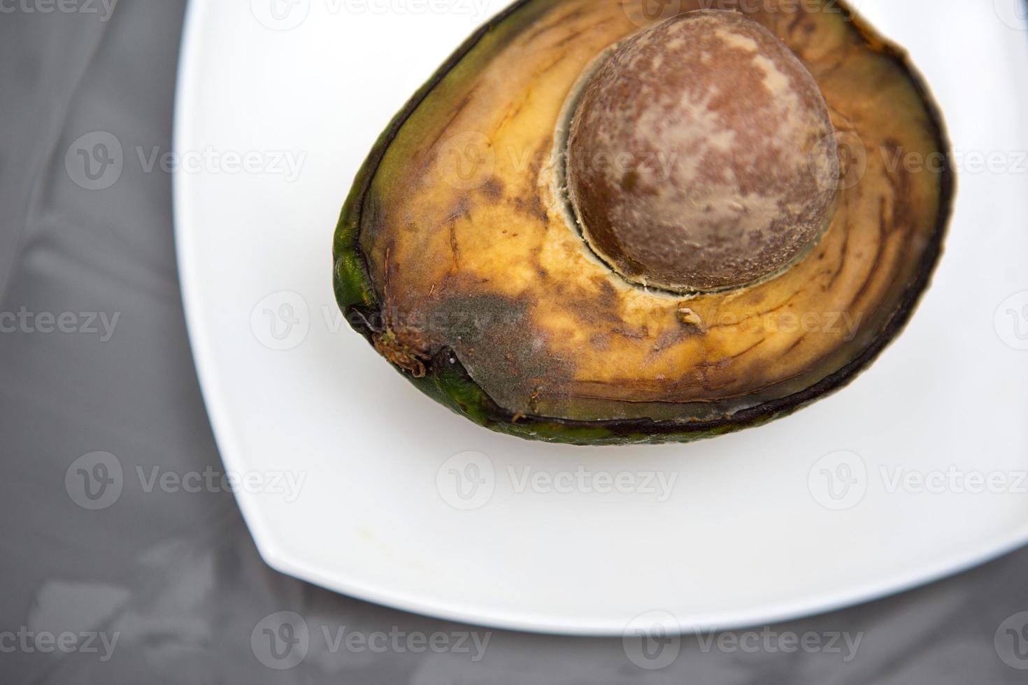 Spoiled avocado with green mold and black spots of rot and fungus on a gray background. Cut natural fruit, half with a round bone. Space for text photo