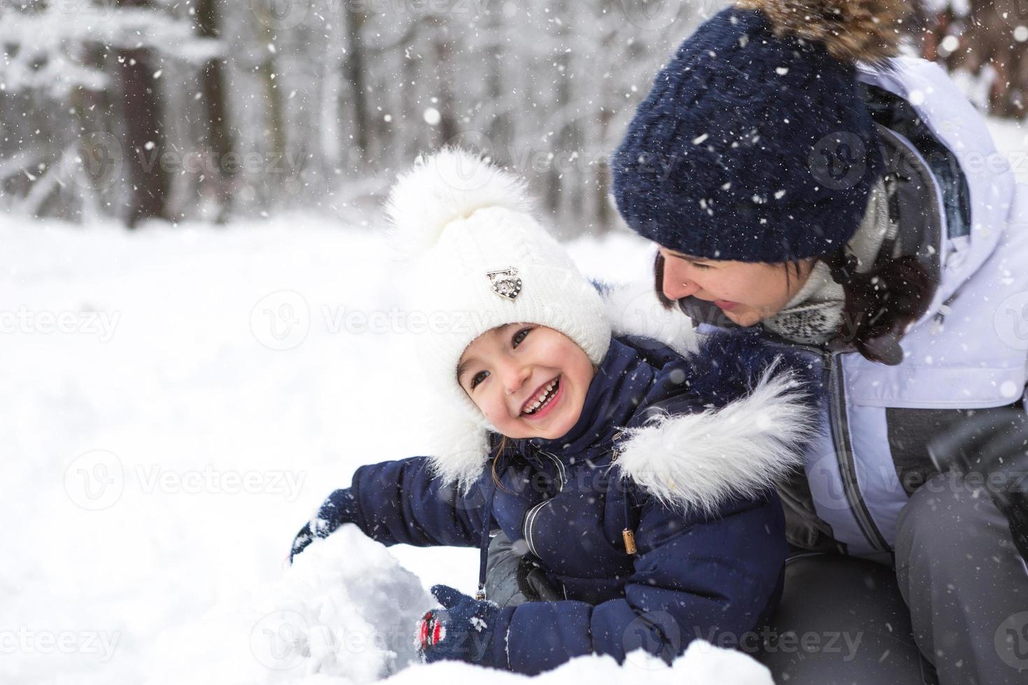 Mom and daughter play snow games, build a fortress, make snowballs. Winter entertainment outside, active recreation, fun in the cold in warm clothes. Outdoor recreation, fun childhood, strong family photo