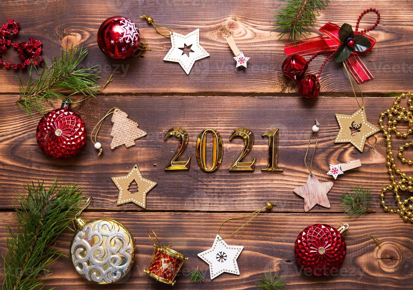 Christmas flat lay with new year 2021 symbol of gold numbers in the center. Holiday atmosphere, wooden stars, toys, beads, red balls, spruce branches on a dark background. Space for text photo