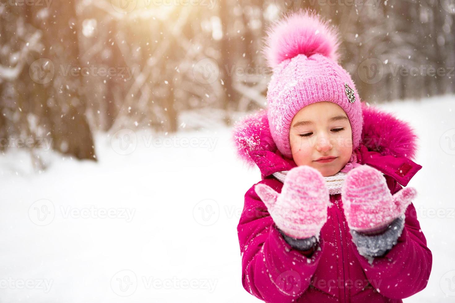 niña en el frío mira los mitones de nieve y sonríe. invierno, pasear al  bebé al