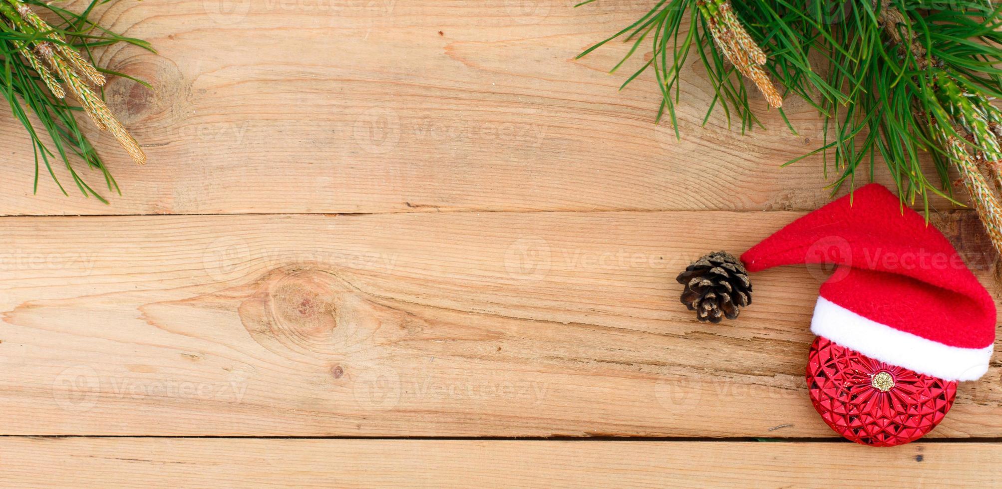 Red Christmas ball, green pine branch with cones on a wooden background. The concept of new year and Christmas, warm knitted things, Santa Claus hat. Flatlay, top view photo