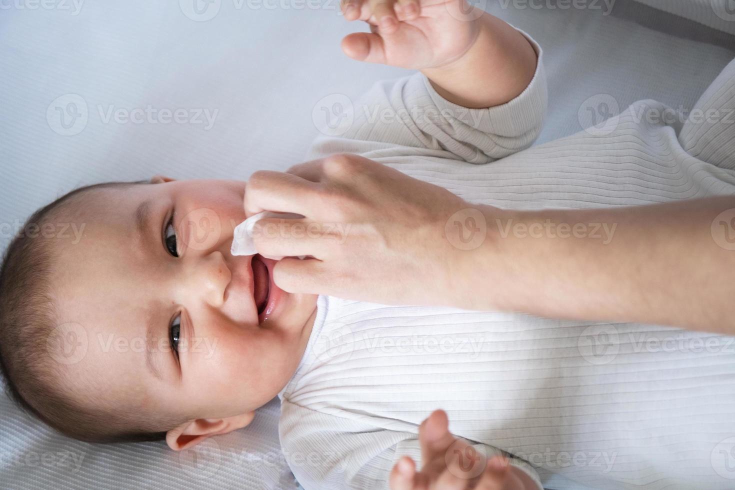 Mom wipes the baby's drool with a napkin. Baby care, teething, drooling. photo