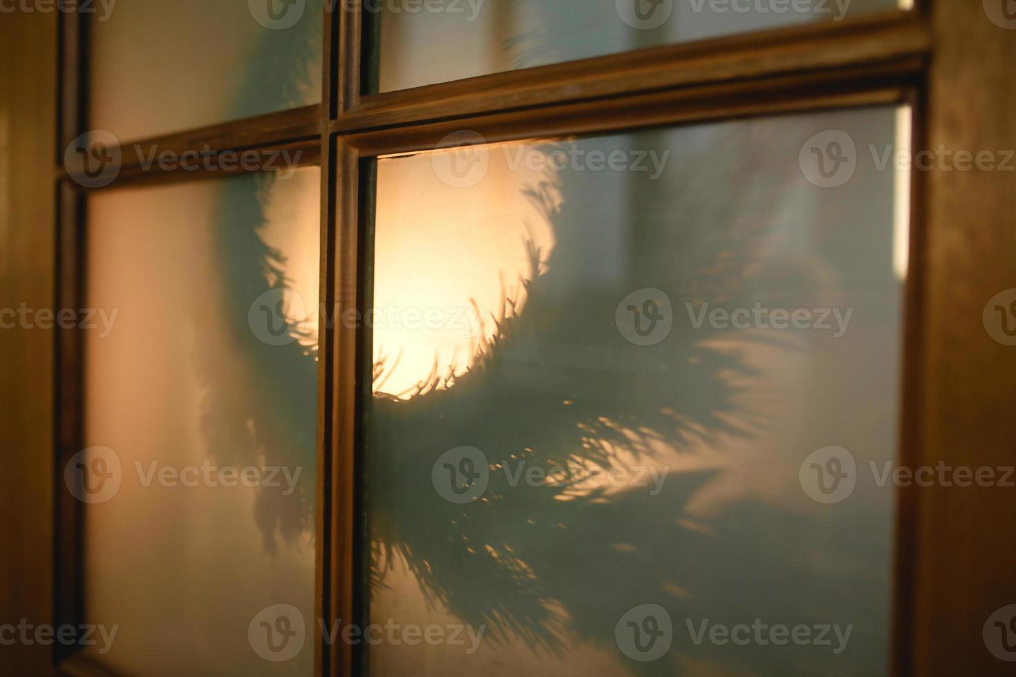 A Christmas wreath is seen from the outside through the glass window of a wooden door with a yellow light. New year, home decoration on the inside. photo