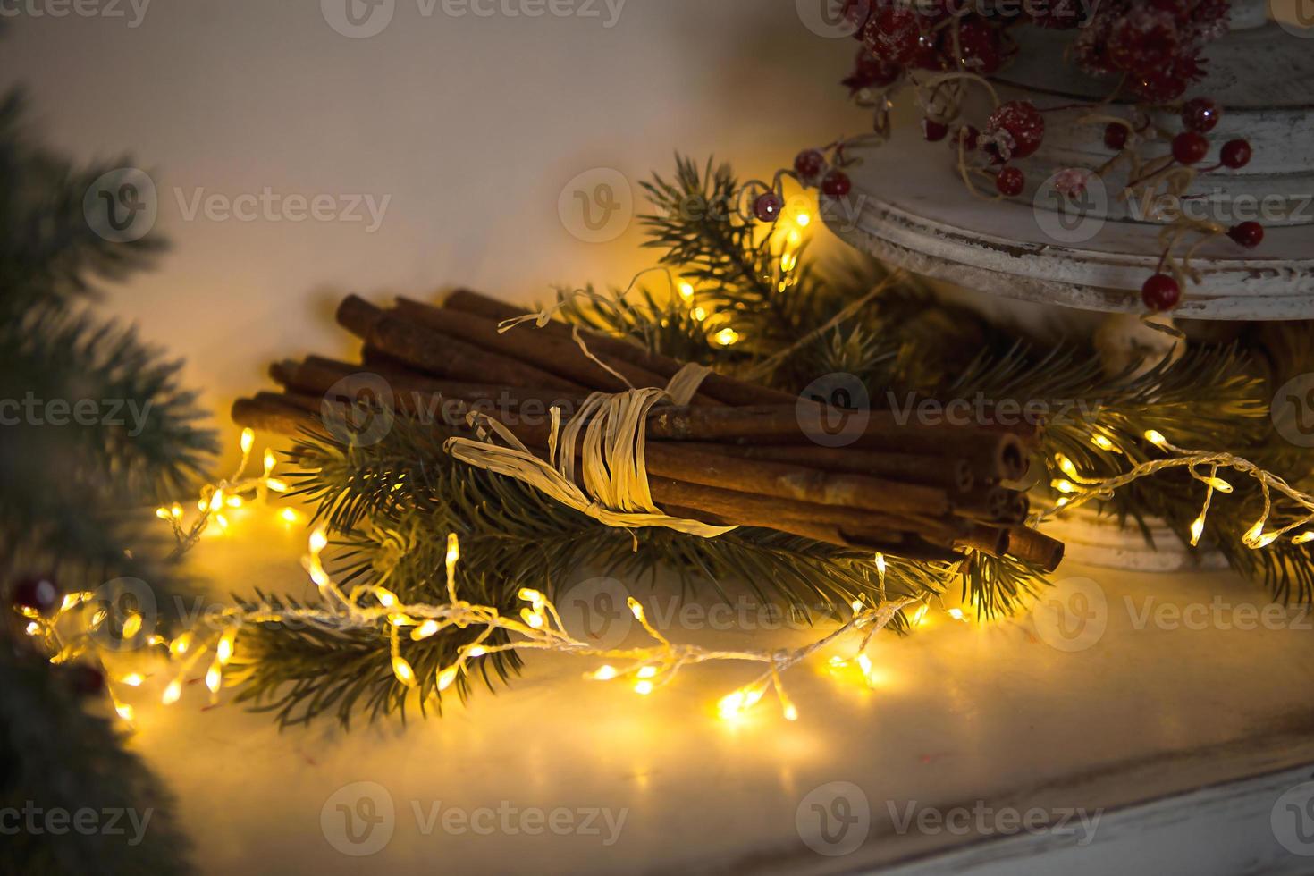 Cinnamon sticks tied with string in yellow lights garlands on Christmas tree branches and red berries. The atmosphere of the new year festive background, details of decorations photo