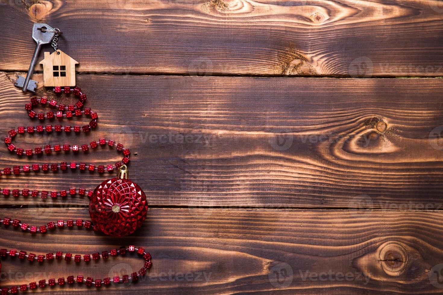 Key to the house with a keychain on top of Christmas tree made of red square beads. Flat lay on wooden background. Building or buying a house in new year. Mortgage, real estate rental. Space for text photo