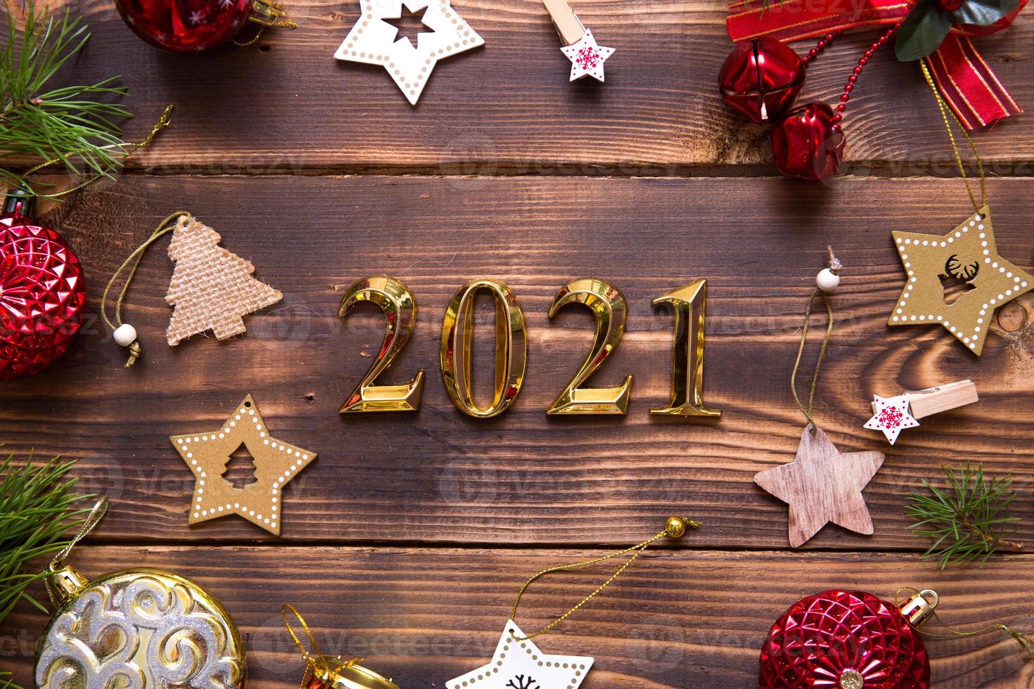 Christmas flat lay with new year 2021 symbol of gold numbers in the center. Holiday atmosphere, wooden stars, toys, beads, red balls, spruce branches on a dark background. Space for text photo