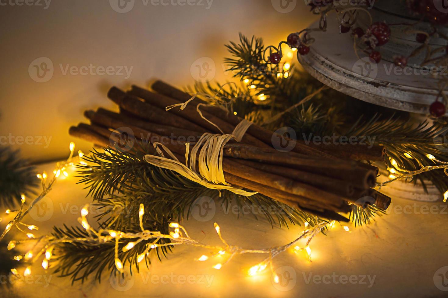 Cinnamon sticks tied with string in yellow lights garlands on Christmas tree branches and red berries. The atmosphere of the new year festive background, details of decorations photo