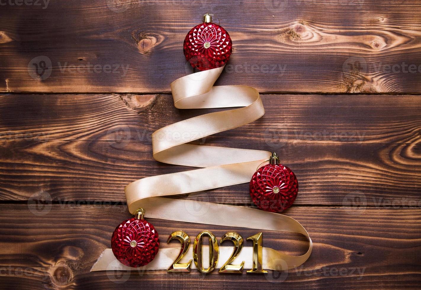 A Christmas tree made of gold ribbon with the numbers 2021 is decorated with red balloons on a dark wooden background. Flat lay. Space for text. New year, Santa hat. photo