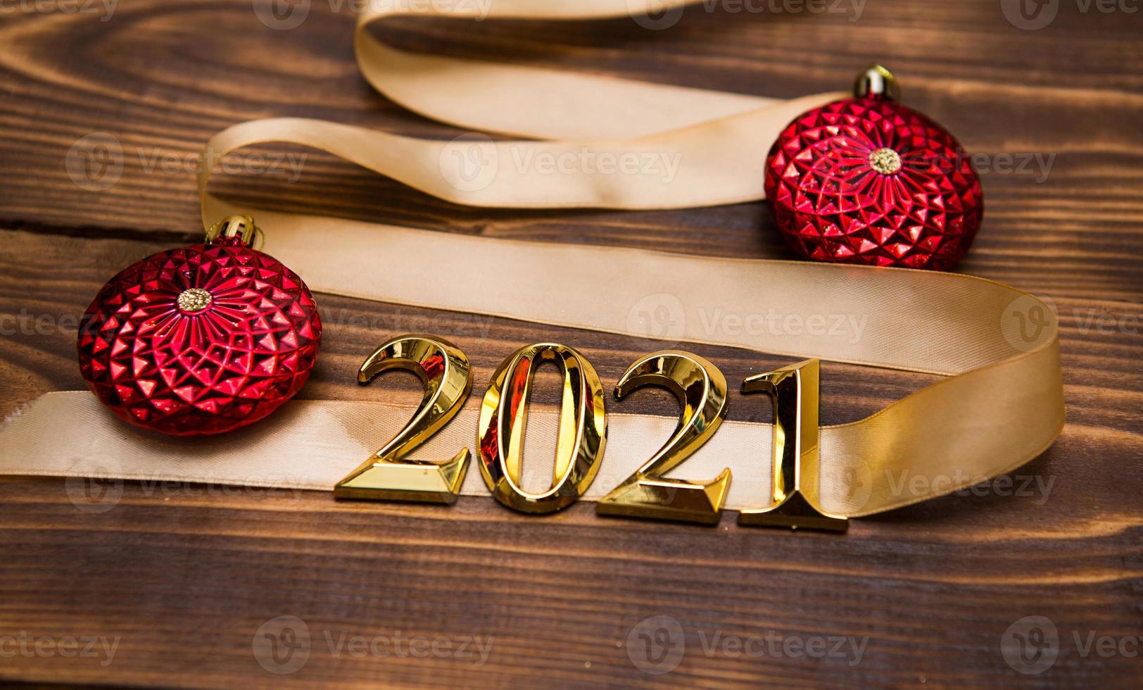 A Christmas tree made of gold ribbon with the numbers 2021 is decorated with red balloons on a dark wooden background. Flat lay. Space for text. New year, Santa hat. photo