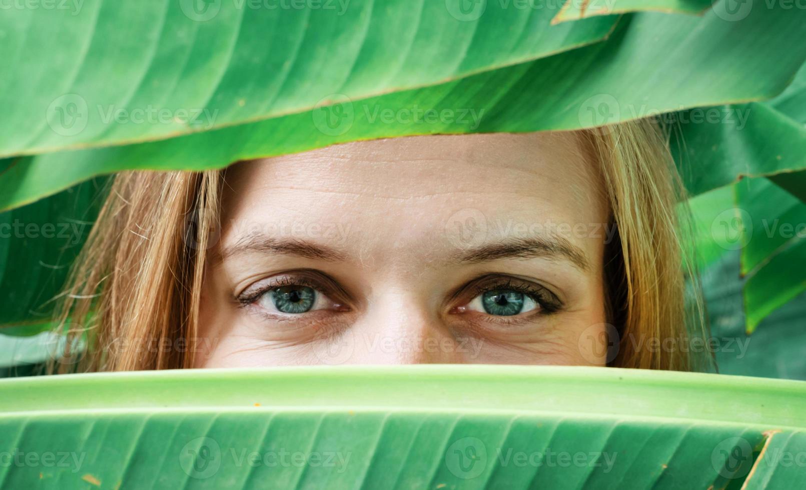 closeup of young woman eyes looking from palm trees leaves photo