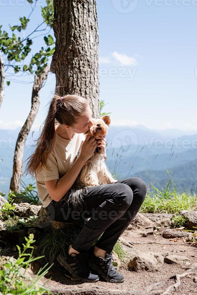 mujer joven sosteniendo un pequeño cachorro de perro yorkshire terrier caminando por las montañas foto