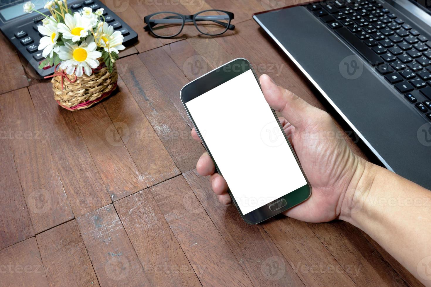 Human hand holding mobile smart phone and office equipment on desktop photo