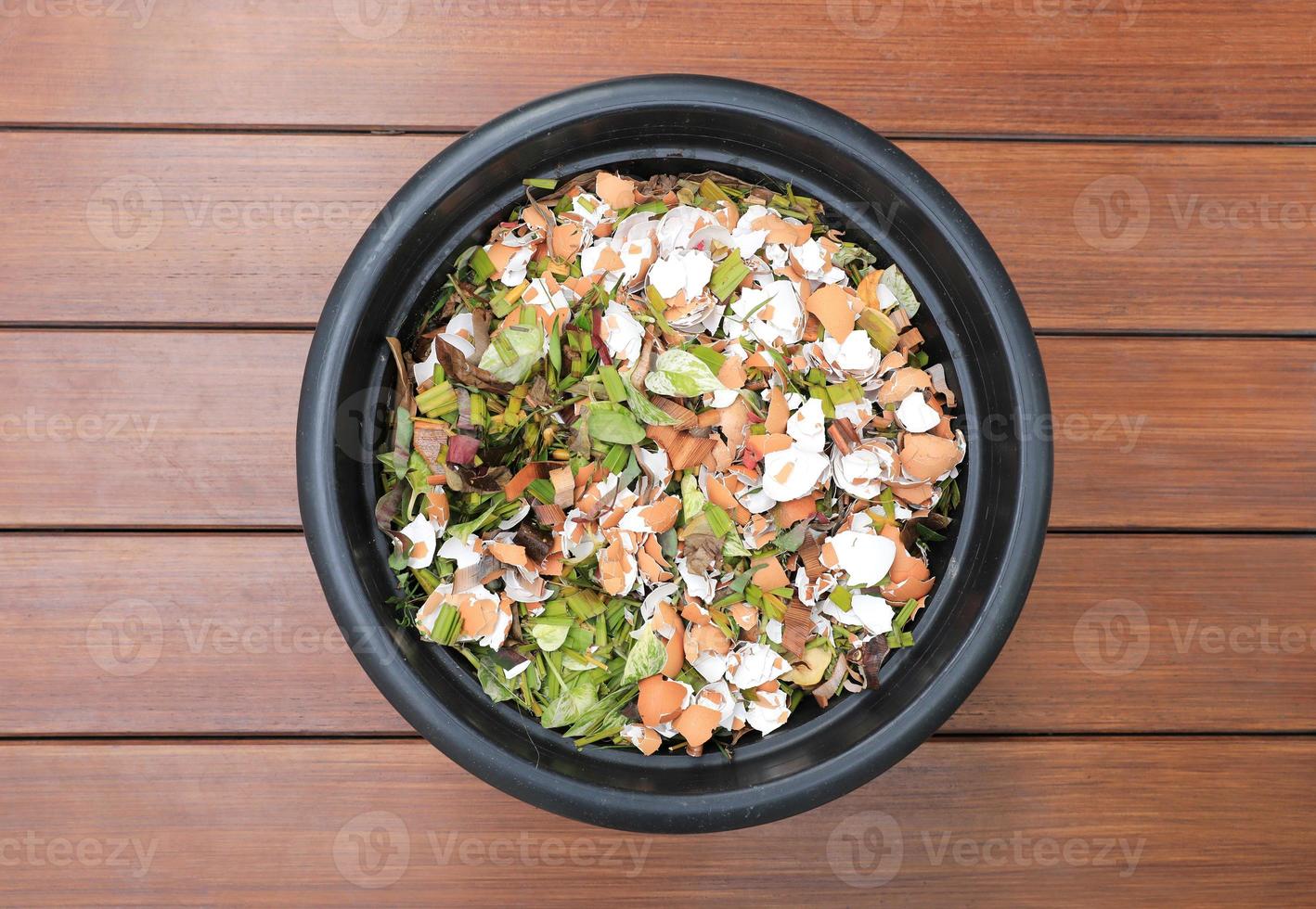 Composting pile of leaves and rotting kitchen scraps with eggshells garbage waste in black bucket on wooden floor.. photo