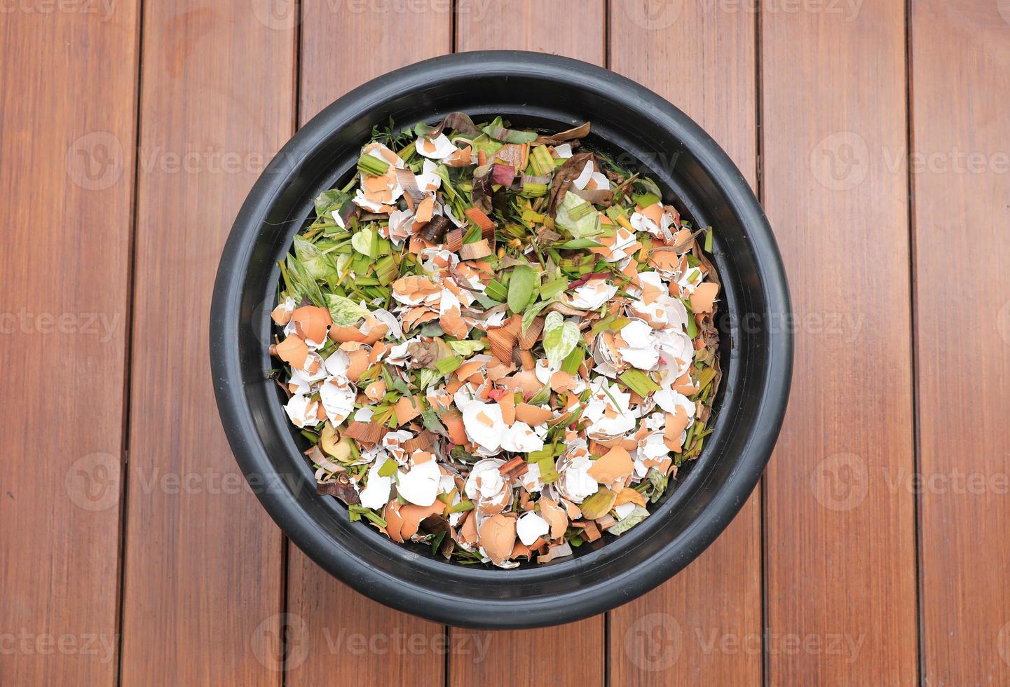 Composting pile of leaves and rotting kitchen scraps with eggshells garbage waste in black bucket on wooden floor.. photo