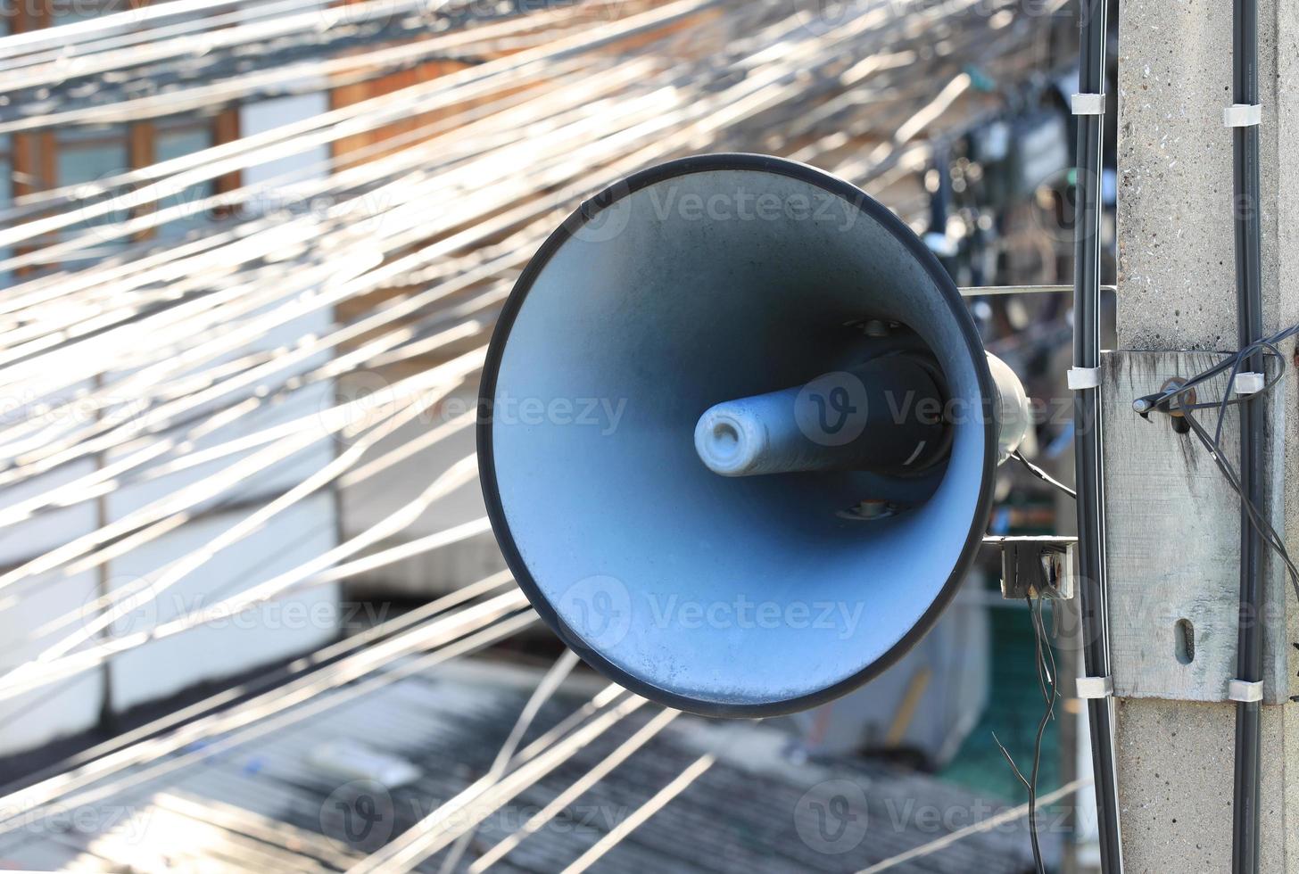 Vintage horn loudspeaker installed on the pole with messy wires in background. photo