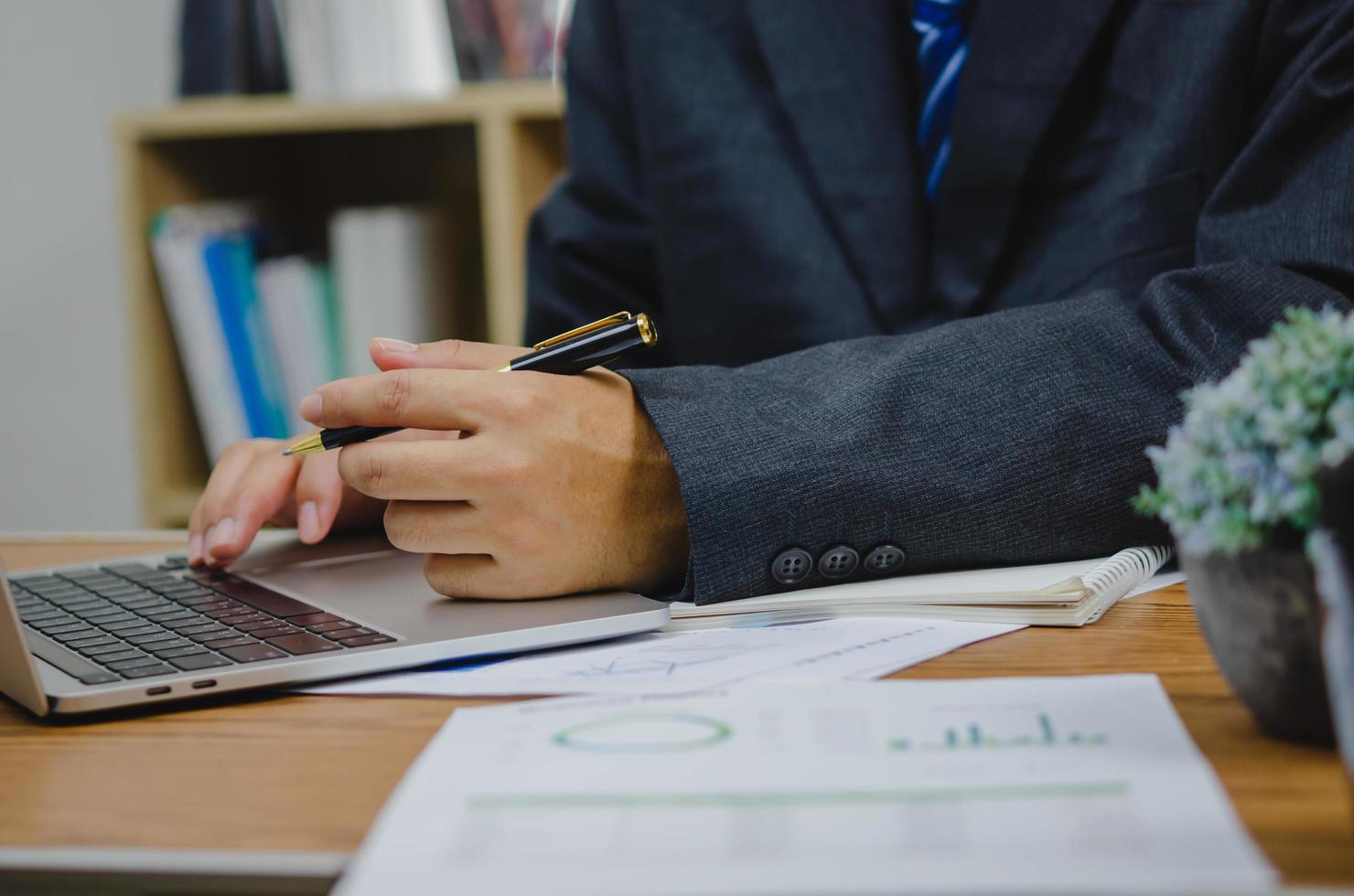 Businessman holding pen document graph accounting finance paper work analysis chart marketing investment and report economy with computer laptop on desk at office. photo