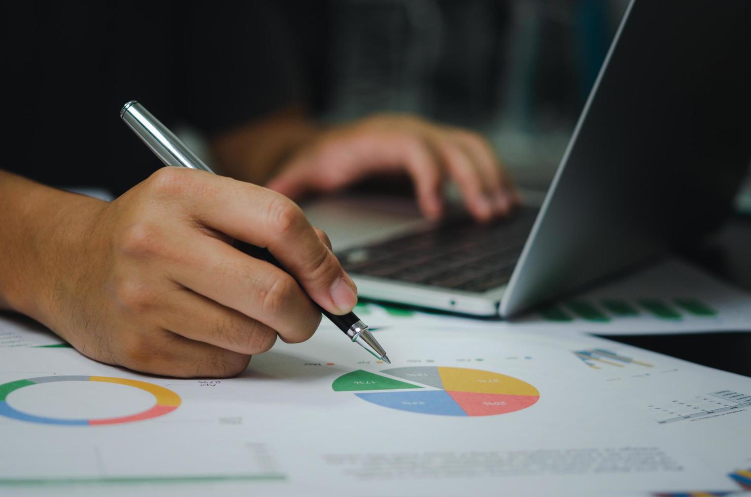 Businessman holding pen document graph accounting finance paper work analysis chart marketing investment and report economy with computer laptop on desk at office. photo