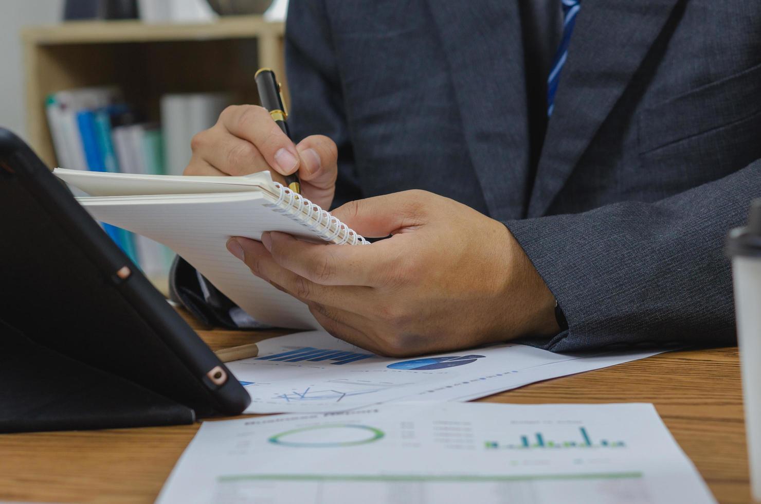 Businessman holding pen document graph accounting finance paper work analysis chart marketing investment and report economy with computer laptop on desk at office. photo