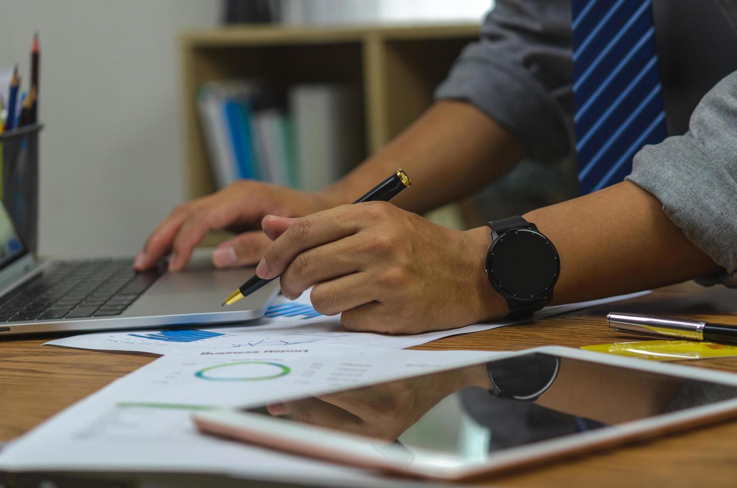 Businessman holding pen document graph accounting finance paper work analysis chart marketing investment and report economy with computer laptop on desk at office. photo