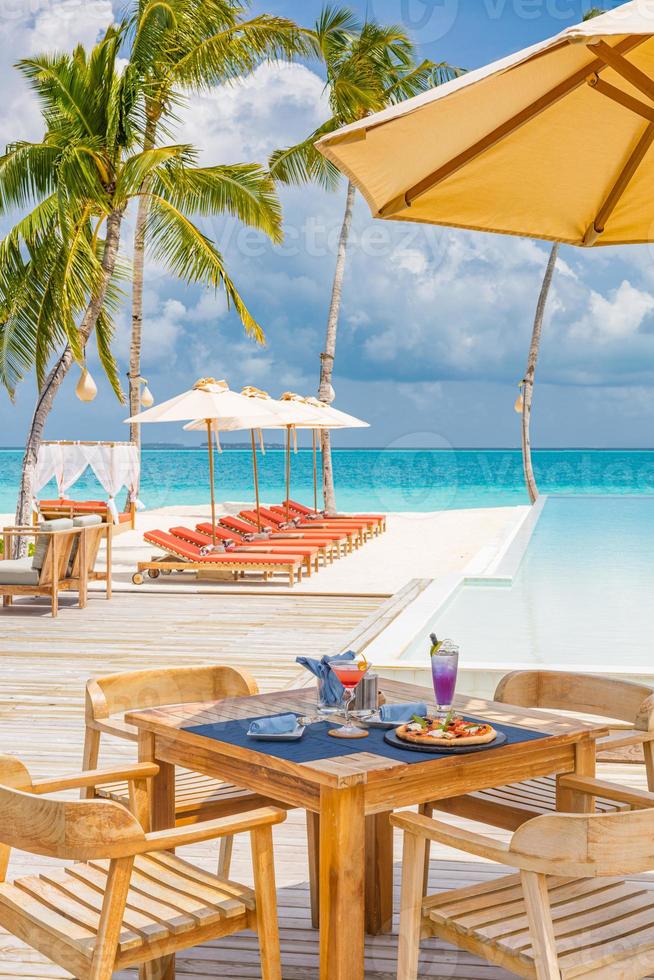 primer plano de la mesa de la mañana, palmeras, cócteles en la piscina infinita en un hotel de lujo junto a la piscina, restaurante al aire libre, playa, océano y cielo, café de la isla tropical. vacaciones de verano o vacaciones, viajes familiares. foto