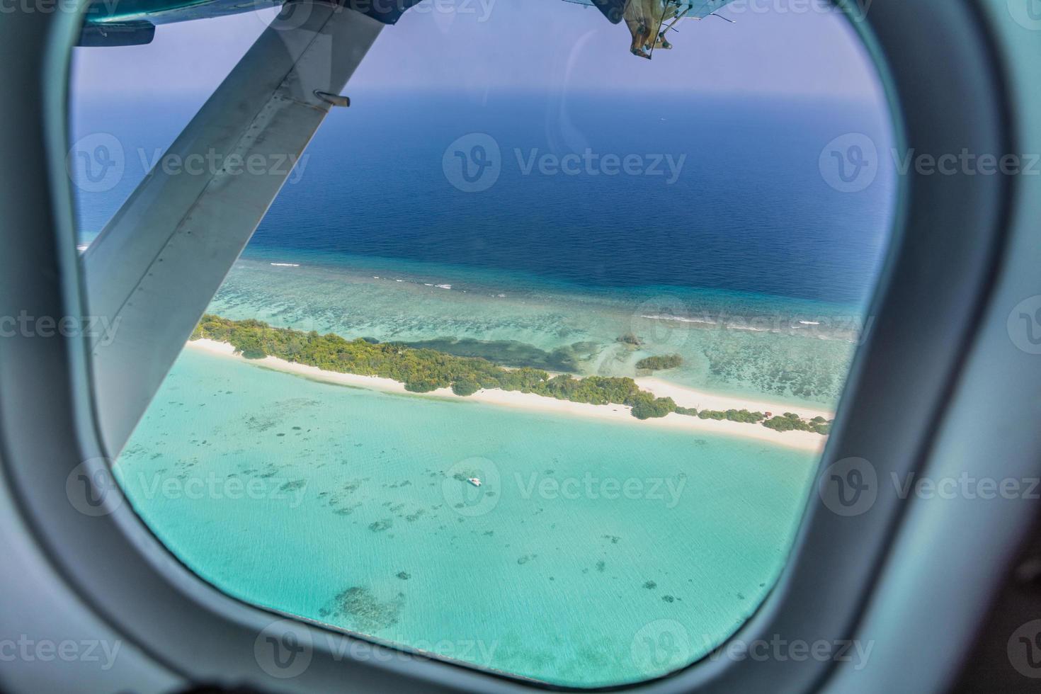 Airplane window with beautiful Maldives island view. Luxury summer holiday travel tourism background, view from airplane window. Atolls and islands with amazing tropical sea photo