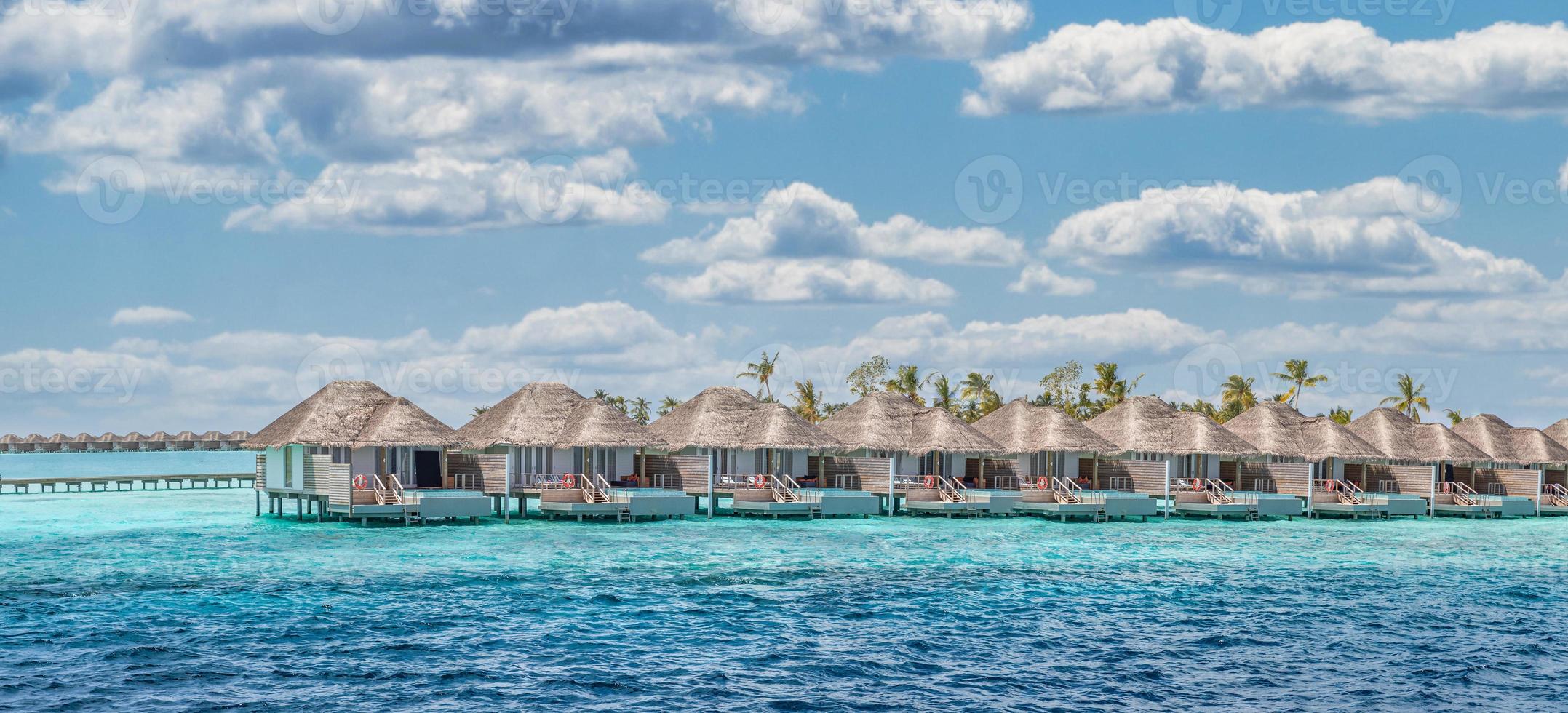 Aerial view of Maldives island, luxury water villas resort and wooden pier. Beautiful sky and ocean lagoon beach background. Summer vacation holiday and travel concept. Paradise aerial landscape pano photo