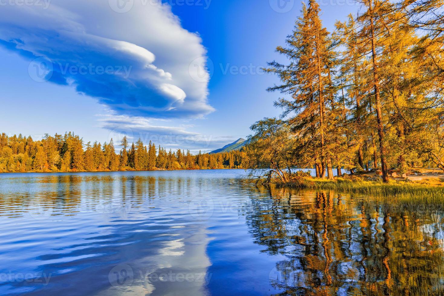 Beautiful golden colored trees with autumn lake landscape. Tranquil autumn sunset. Calm morning view of Strbske pleso lake. Amazing nature outdoor of High Tatra National Park, Slovakia, Europe photo