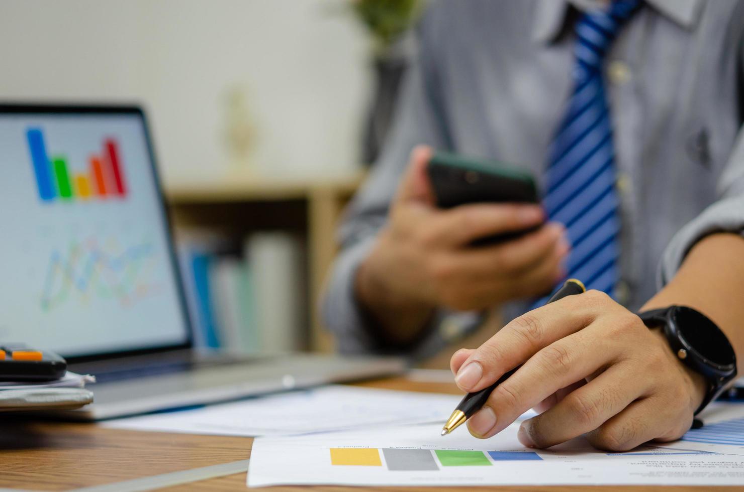 Businessman holding pen document graph accounting finance paper work analysis chart marketing investment and report economy with computer laptop on desk at office. photo
