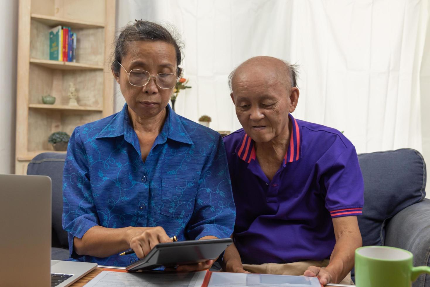 Asian elderly sit and holding calculator for insurance or medical expenses and a computer on desk home. photo