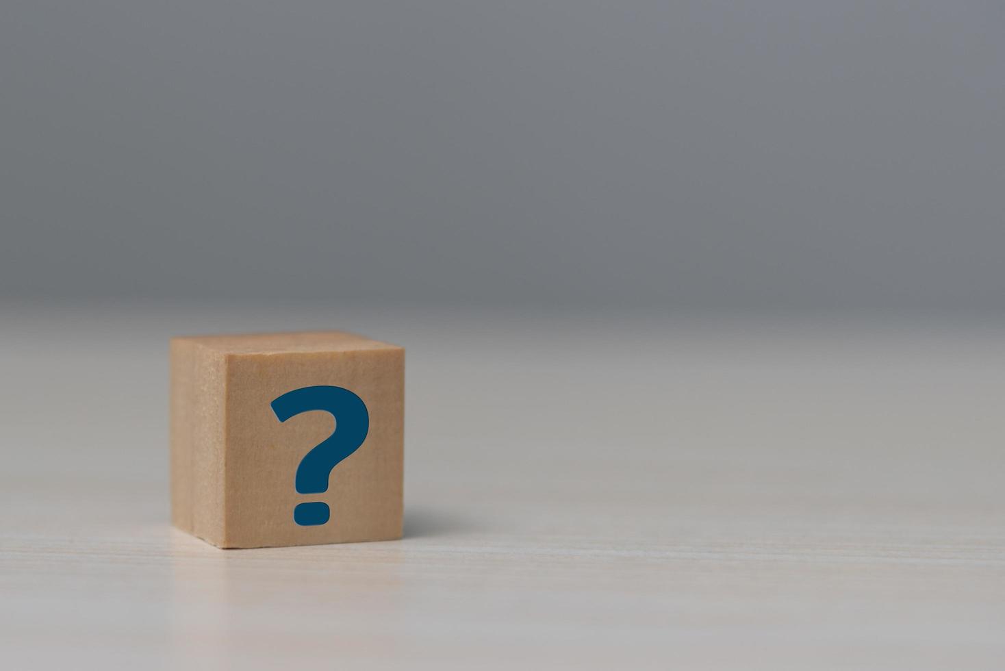 Wooden cube block shape with sign question mark symbol on table. photo