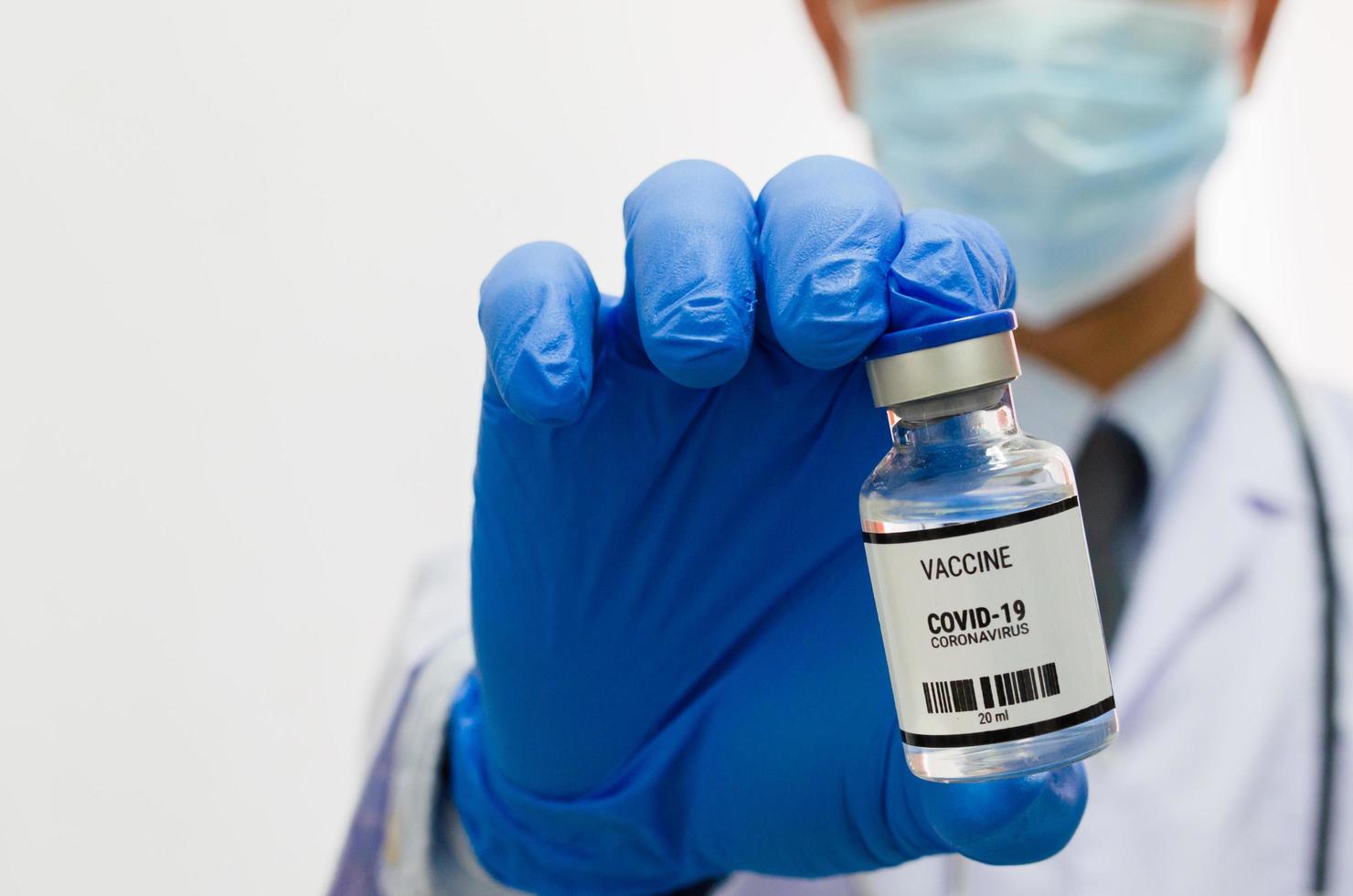 médico masculino con guantes médicos uniformes sosteniendo una botella de virus de la vacuna covid 19 sobre fondo blanco. copie el espacio. foto