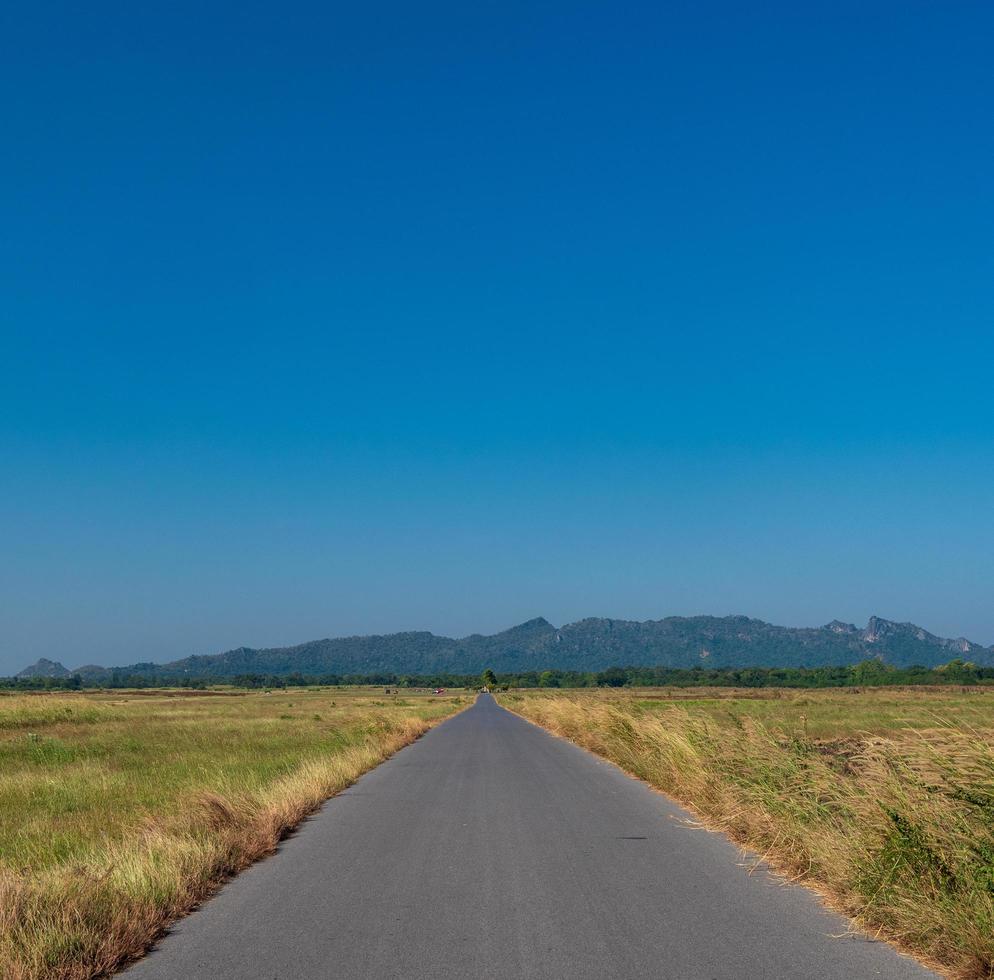 long road that travel through various village in rural Thailand passing through forest meadows and mountain on clear day blue sky white cloud in summer Suitable driving photo