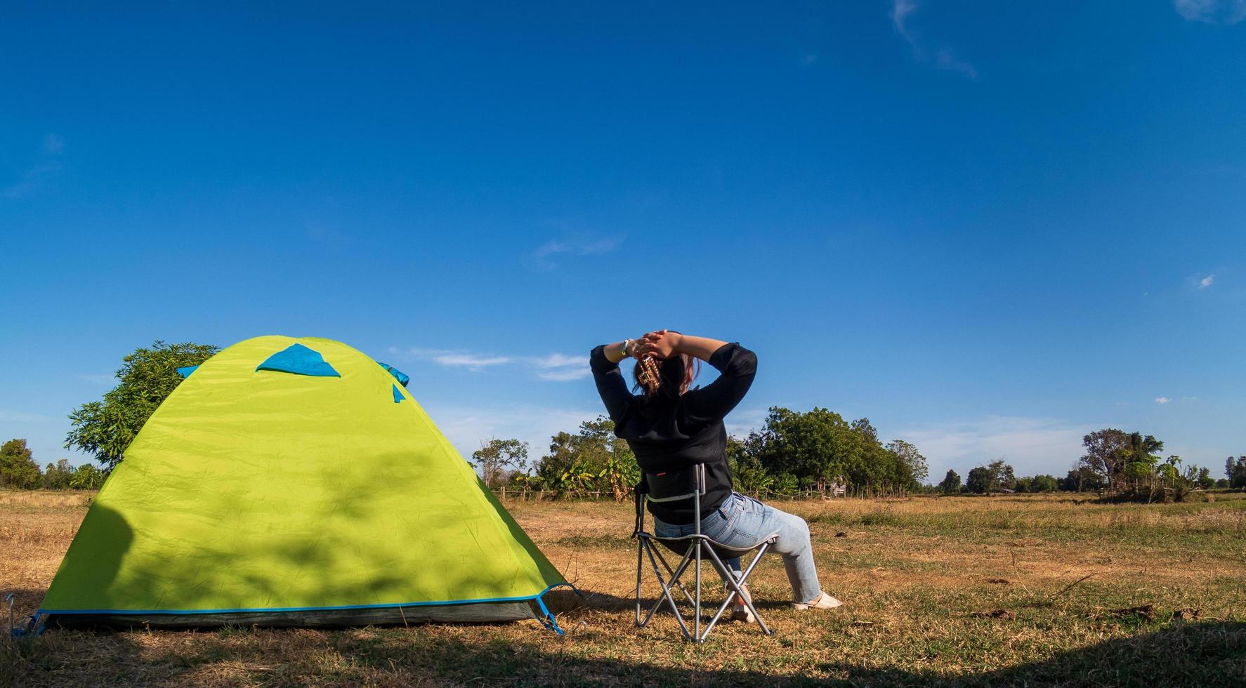 Asian female tourists are sitting happy free with green tent for traveler sits on  wide field, overlooking evening time Of Private area Thailand for camping getaway During long holiday for travel. photo