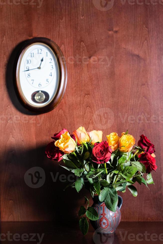 reloj de pared y rosas rojas y amarillas frescas en jarra foto