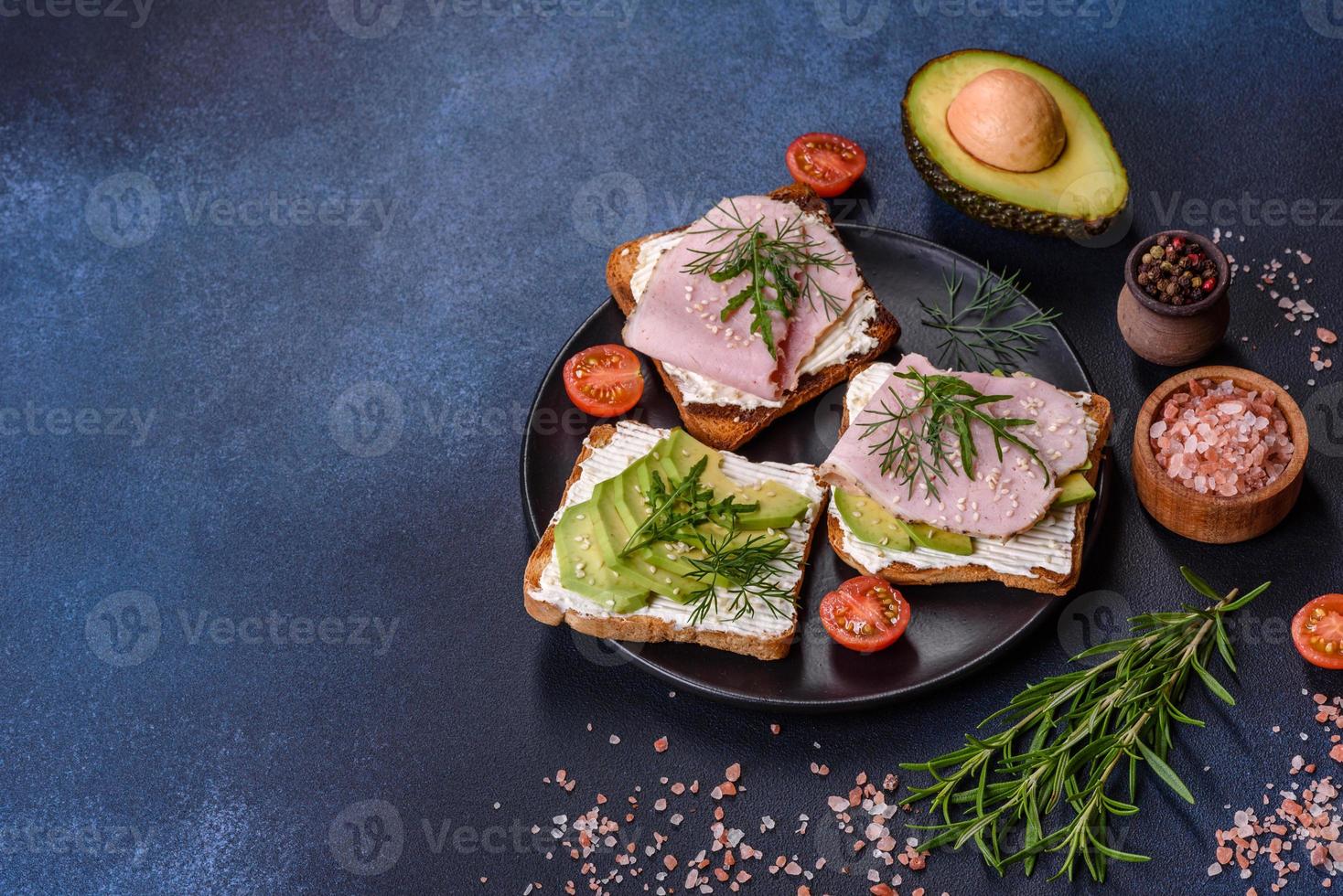 Sándwiches frescos y deliciosos de jamón, mantequilla, aguacate y semillas de sésamo en una tabla de cortar de madera foto