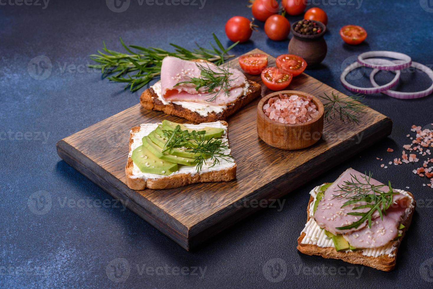 Fresh, delicious ham, butter, avocado and sesame seeds sandwiches on a wooden cutting board photo