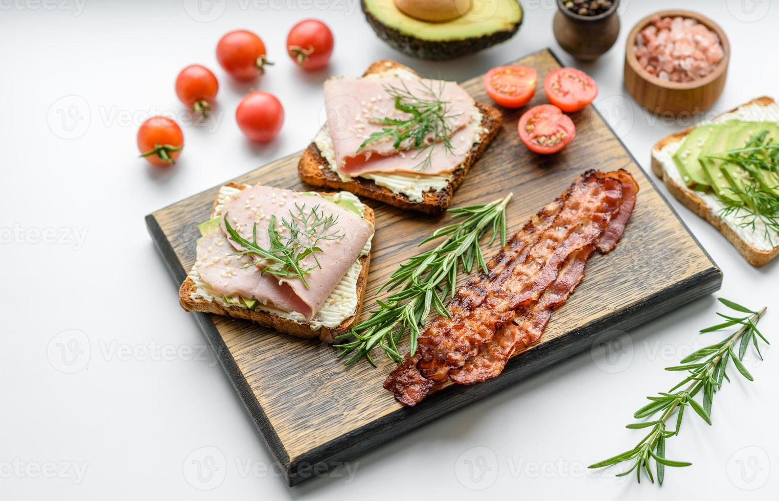 Sándwiches frescos y deliciosos de jamón, mantequilla, aguacate y semillas de sésamo en una tabla de cortar de madera foto