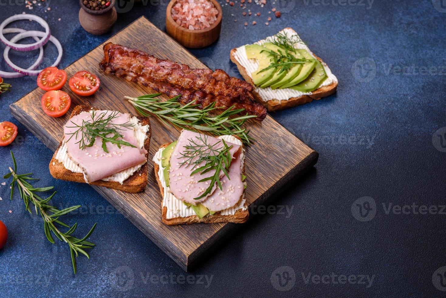 Sándwiches frescos y deliciosos de jamón, mantequilla, aguacate y semillas de sésamo en una tabla de cortar de madera foto