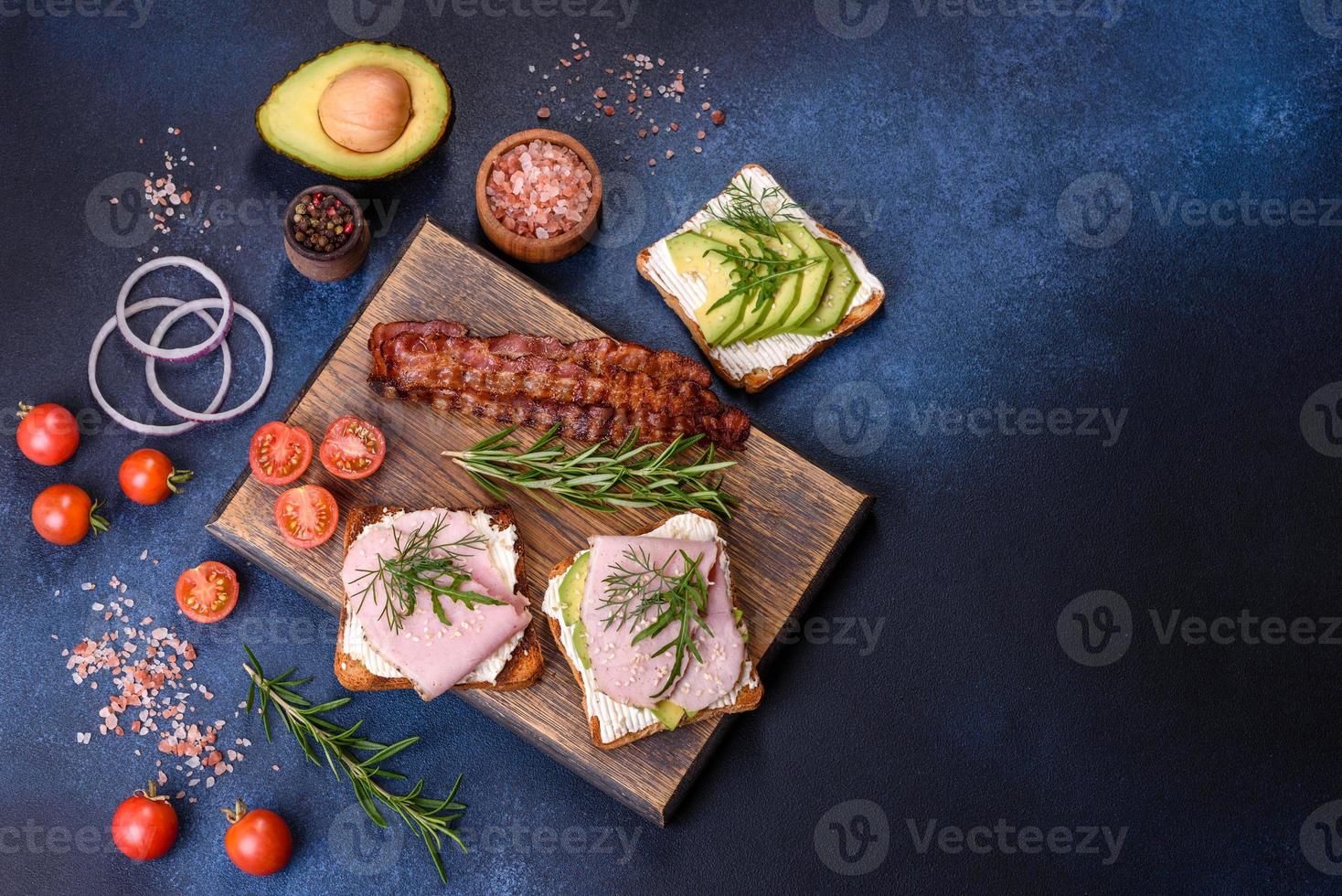 Sándwiches frescos y deliciosos de jamón, mantequilla, aguacate y semillas de sésamo en una tabla de cortar de madera foto