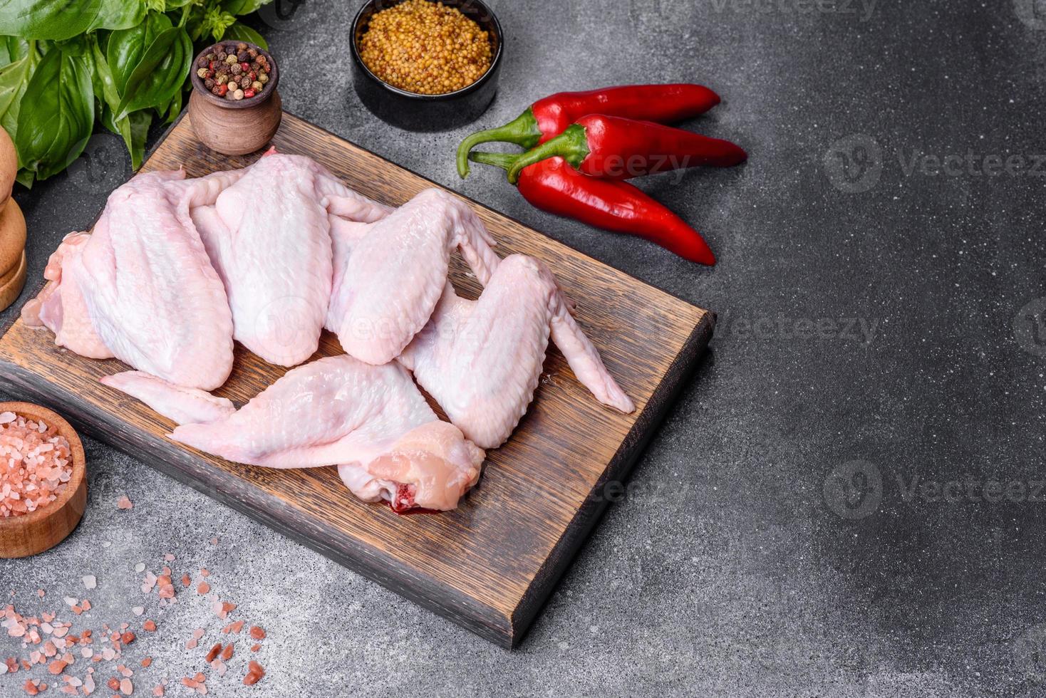 alitas de pollo crudas con ingredientes para cocinar en una tabla de cortar de madera foto