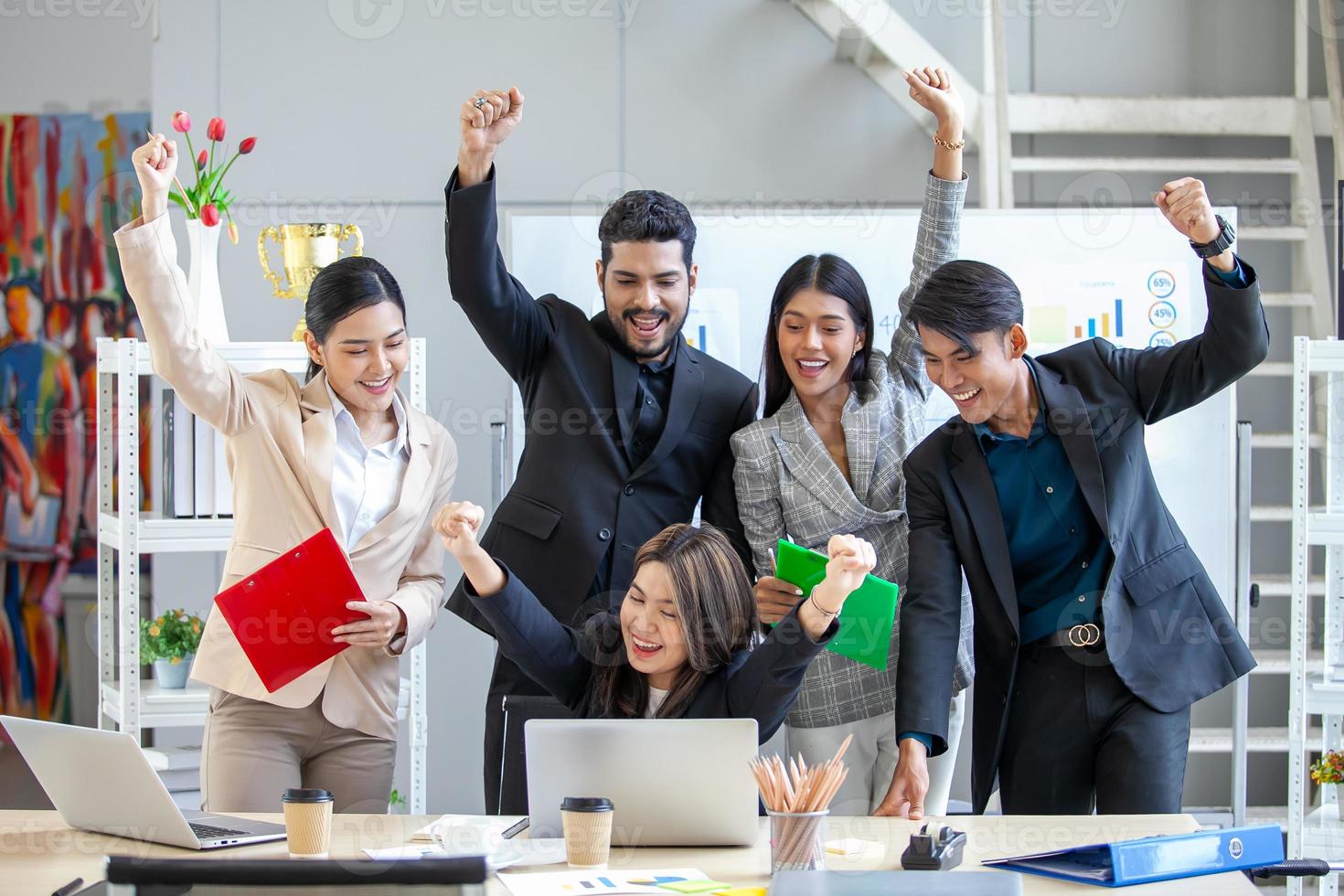 Asian business team celebrate corporate victory together in office, laughing and rejoicing, smiling excited employees colleagues screaming with joy in office. photo